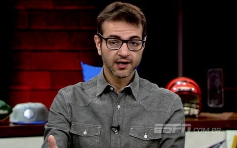 Ari Aguiar usa uma camisa cinza e está no cenário do ESPN League, programa sobre esportes americanos da Disney, que vai ao ar semanalmente