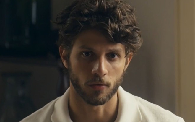 Chay Suede com expressão séria em cena como Ari na novela Travessia