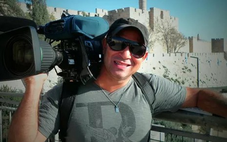 Ari Júnior em 2015, no Nepal, com uma camisa cinza e boné, além de segurar uma câmera durante uma reportagem da Globo