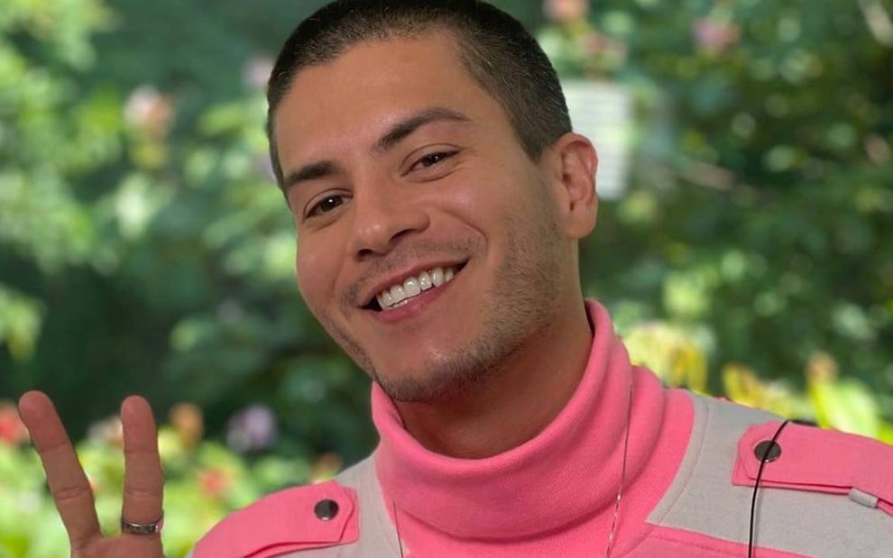 Foto de Arthur Aguiar; ele aparece sorrindo e veste blusa rosa