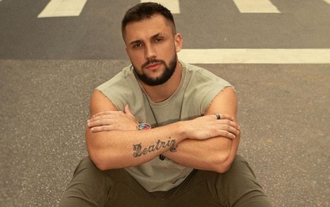Arthur Picoli em foto publicada no Instagram; o modelo está sentado no asfalto, com um semblante sério, braços cruzados e veste uma regata bege