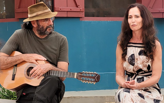 Almir Sater está com violão no colo durante gravação de série com a atriz Ingra Lyberato