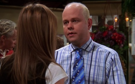 Gunther (James Michael Tyler) de camisa e gravata azuis olha para a esquerda para uma mulher de costas em cena da série Friends