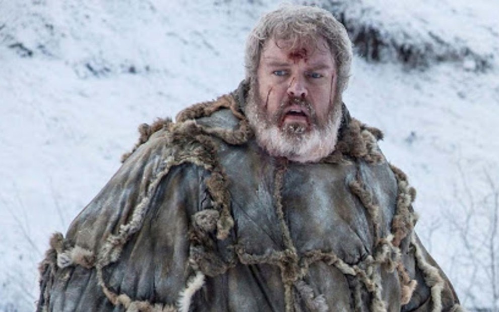 Hodor (Kristian Nairn) com casaco de pele e sangue na testa em cenário de montanha com neve ao fundo em cena da série Game of Thrones