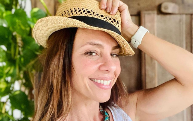 Carla Marins sorri para foto segurando um chapéu na cabeça em foto publicada no seu perfil no Instagram
