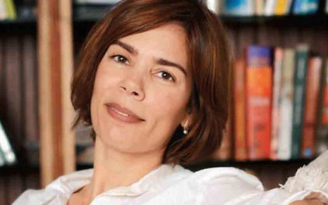 Andrea Maltarolli posa de camisa branca, em frente a uma estante de livros