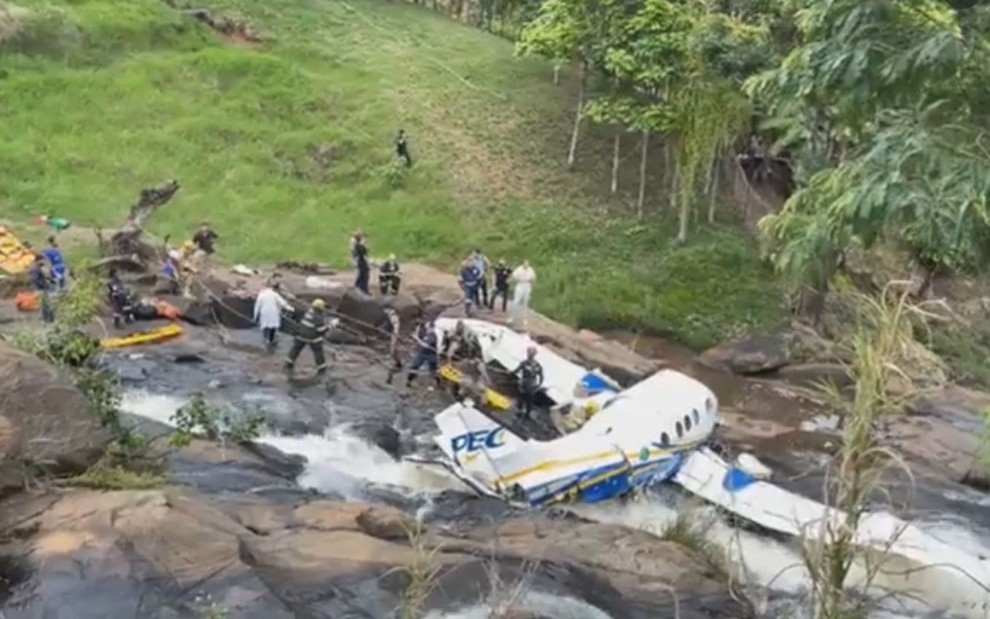 Avião destroçado sobre pedras e riacho em ambiente rural