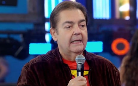Faustão nos estúdios da Globo, usando uma jaqueta de cor preta com uma blusa vermelha, apresentado o seu antigo programa dominical