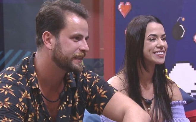 Gustavo Marsengo e Larissa Tomásia olhando para a televisão na casa de vidro do BBB 22