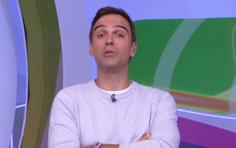 Tadeu Schmidt está de braços cruzados e usa um agasalho lilás enquanto apresenta o BBB 22, da Globo