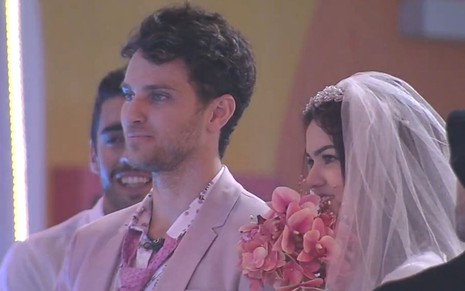 Eslovênia Marques usando véu de noiva e segurando um buquê de flores ao lado de Lucas Bissoli durante festa do líder