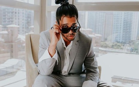 Luciano Estevan em foto publicada no Instagram; ele está sentado e veste um terno cinza, camisa branca e óculos escuros