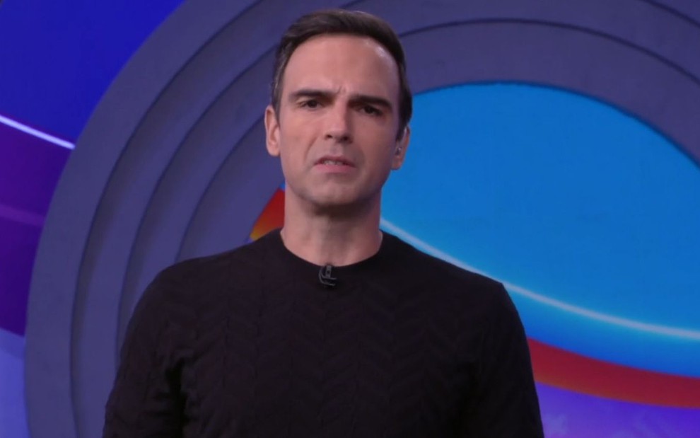Tadeu Schmidt veste blusa preta enquanto apresenta o BBB 22 na Globo