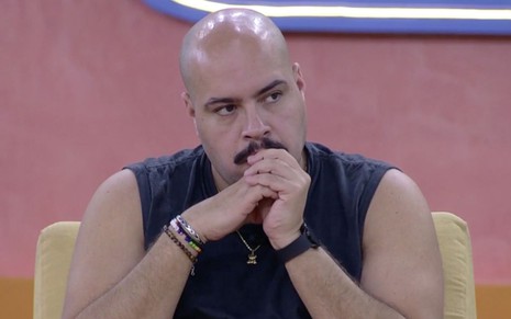 Tiago Abravanel quando ainda estava no Big Brother Brasil 22: cantor estava sentado, com regata preta e coloca as mãos perto da boca