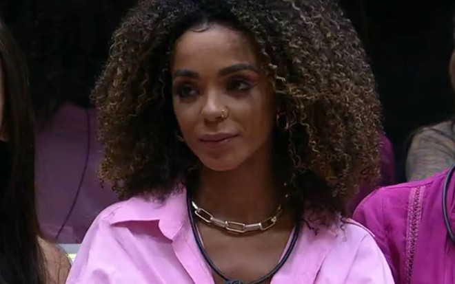 Brunna usa camiseta rosa, está com o cabelo solto e usa microfone preto