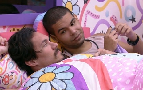 Imagem de Eliezer Netto (à esq.) e Vinicius Fernandes deitados na cama de casal do quarto Lollipop no BBB 22