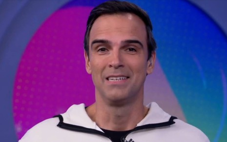 Tadeu sorri e veste blusa branca enquanto apresenta o BBB 22 na Globo