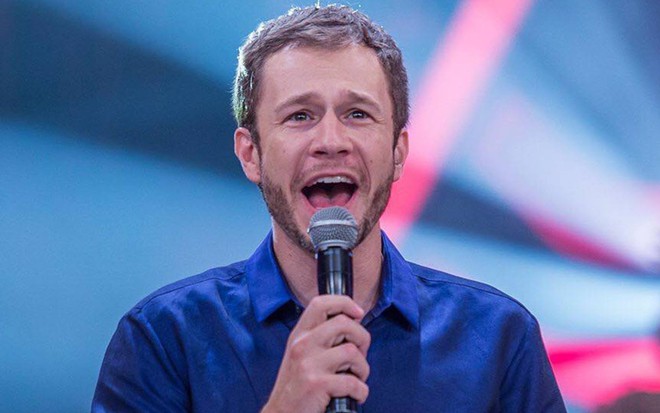Tiago Leifert segura microfone e veste camiseta azul