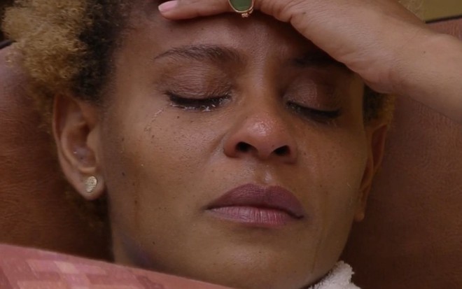 Aline Wirley está de olhos fechados, com uma mão na cabeça e chora no quarto deserto do BBB 23
