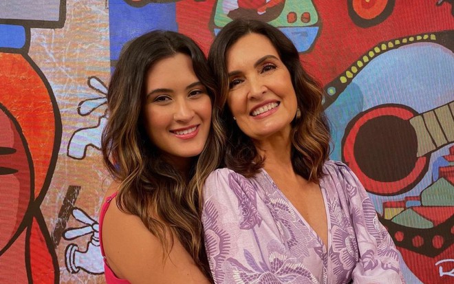 Fátima Bernardes de rosto colado com a filha Beatriz Bonemer; ambas vestem roupas coloridas