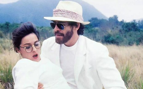 Os atores Maria Zilda Bethlem e José de Abreu em Bebê a Bordo; ela está no colo dele, olhando para baixo com a boca aberta, enquanto ele a segura, de óculos de sol, olhando para baixo