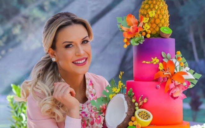 Imagem de Beca Milano ao lado de um bolo colorido feito por ela