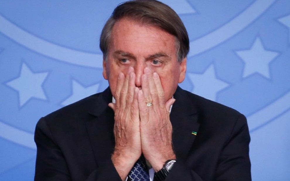 Jair Bolsonaro com as mãos no rosto, mostrando desespero, em um evento em Brasília