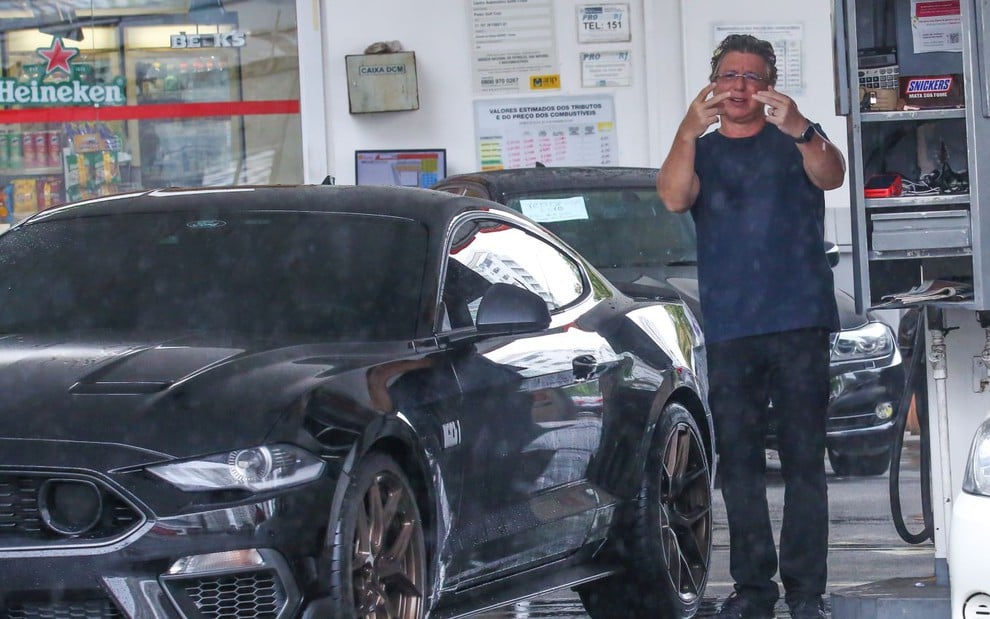 Boninho sinaliza para fotógrafo em posto de gasolina ao lado de seu Ford Mustang Mach 1