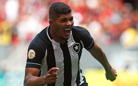 Jogador Erison, do Botafogo, grita ao comemorar gol e veste uniforme listrado em preto e banco
