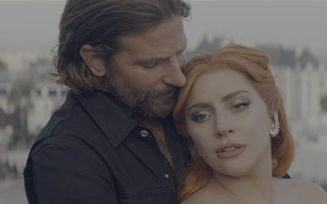Bradley Cooper abraçado a Lady Gaga por trás, enquanto ela, maquiada, olha para o lado