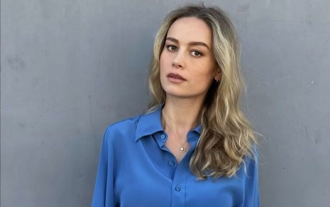 Brie Larson usa blusa azul e posa em fundo cinza