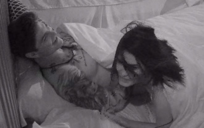 David Kneip e Kethellen Avelino em uma cama, em um quarto com a luz apagada