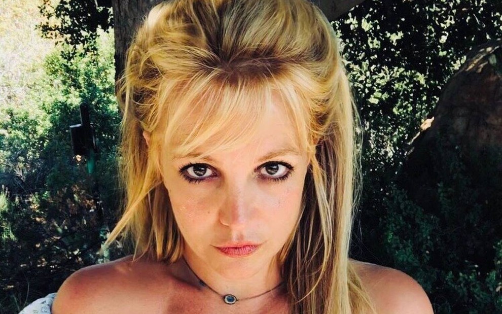 Britney Spears posa em meio ao ar livre; há um fundo verde na imagem