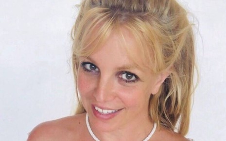 Britney usa blusa branca, está com o cabelo preso e sorri