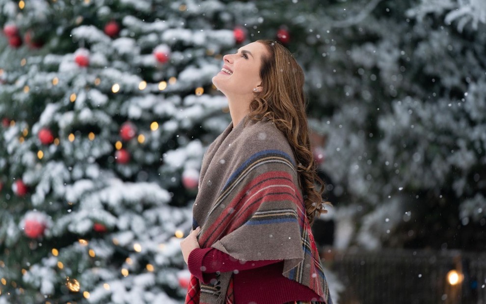 Brooke Shields olha para cima e observa flocos de neve caindo do céu em cena do filme Um Castelo para o Natal