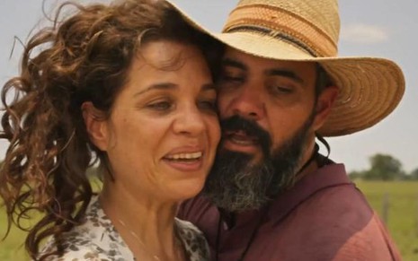 A atriz Isabel Teixeira e o ator Juliano Cazarré como Maria Bruaca e Alcides em Pantanal; ela está olhando para o lado com cara de feliz, enquanto ele, ao seu lado, a abraça com cara provocante