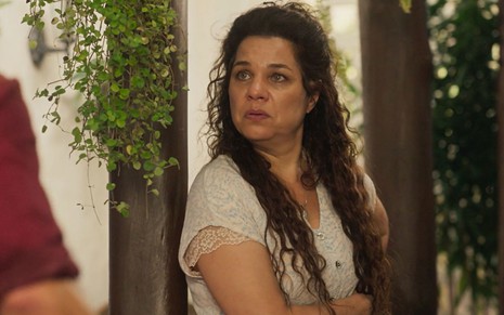 A atriz Isabel Teixeira como Maria Bruaca em Pantanal; ela está de braços cruzados olhando para o lado com cara de dúvida