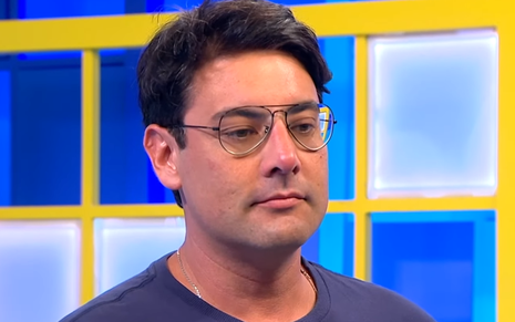 Foto de Bruno de Luca; ele veste camiseta azul e está na frente de um fundo azul