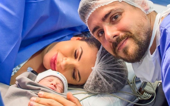 Cacau Colucci está deitada numa mesa cirúrgica, o bebê Arthur é colocado próximo ao rosto dela; Bruno Lima aparece ao lado em foto publicada no Instagram