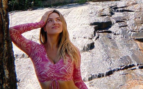 Giovanna Ewbank apoia o braço direito em árvore em paisagem de cachoeira