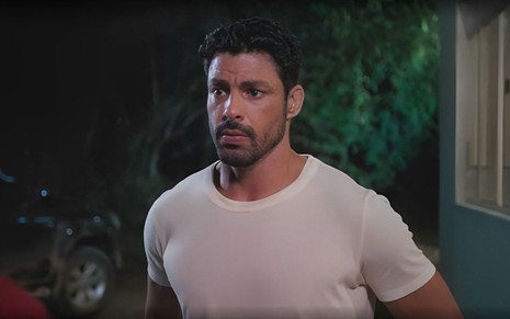 Em cena de Terra e Paixão, Cauã Reymond está com a expressão séria, falando com alguém; ele usa blusa branca