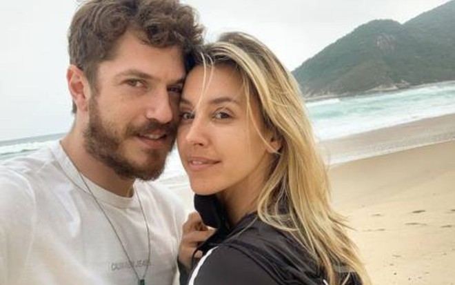 O casal Caio Paduan e Cris Dias com rostos colados, em foto tirada numa praia