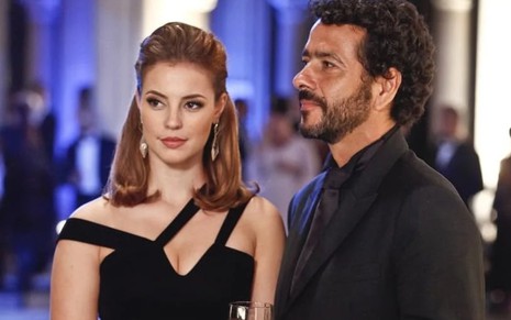 Paolla Oliveira ao lado de Marcos Palmeira em cena da novela Cama de Gato; ambos de preto, ela de vestido e ele de terno e gravata