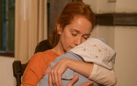 Camila Morgado está com os olhos fechados e segura bebê no colo em cena como Irma na novela Pantanal