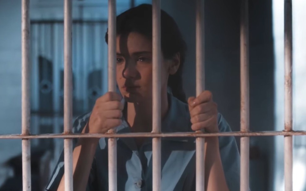 Camila Queiroz está com as mãos nas grades de uma cela e aparece com os olhos marejados em teaser da novela Amor Perfeito