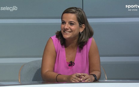 Camila Carelli sorri com uma camisa rosa no Seleção SporTV