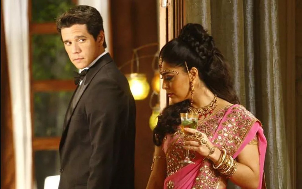 Os atores Marcio Garcia e Juliana Paes como Bahuan e Maya em Caminho das Índias; ele está virado de lado, olhando para trás e observando a colega de cena, que de lado, olha para frente com uma taça na mão