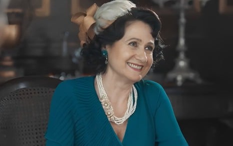 A atriz Zezé Polessa sorrindo, caracterizada como Cândida em cena de Amor Perfeito