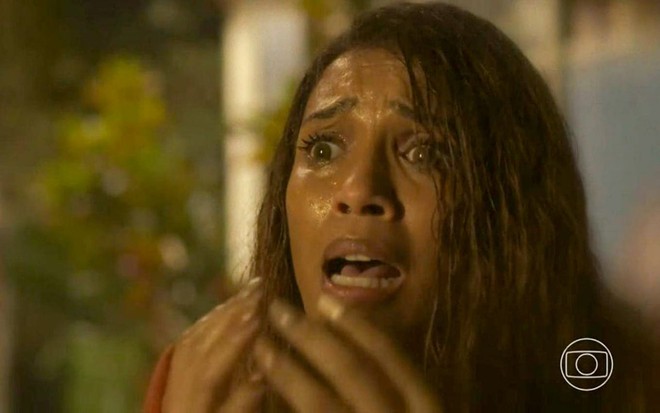 A atriz Taís Araujo como Anita em Cara e Coragem; ela está com os cabelos molhados, levando as mãos na direção à boca e cara de assustada
