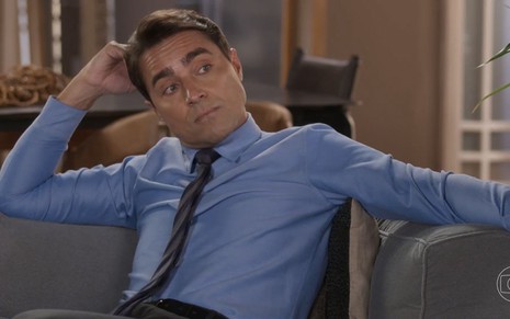 O ator Ricardo Pereira como Danilo em Cara e Coragem; ele está sentado, olhando para o lado com cara de dúvida, enquanto apoia o braço direito no sofá e a mão na cabeça